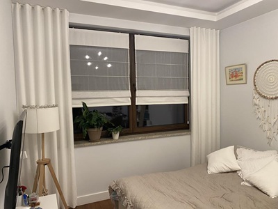 Modernes Schlafzimmer mit cremefarbenen Vorhängen und transparenten Raffrollos